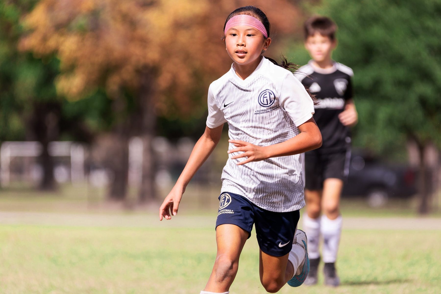 A GFI Academy player running with the ball in a white kit